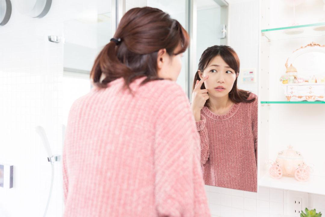 吹き出物を鏡で見る女性